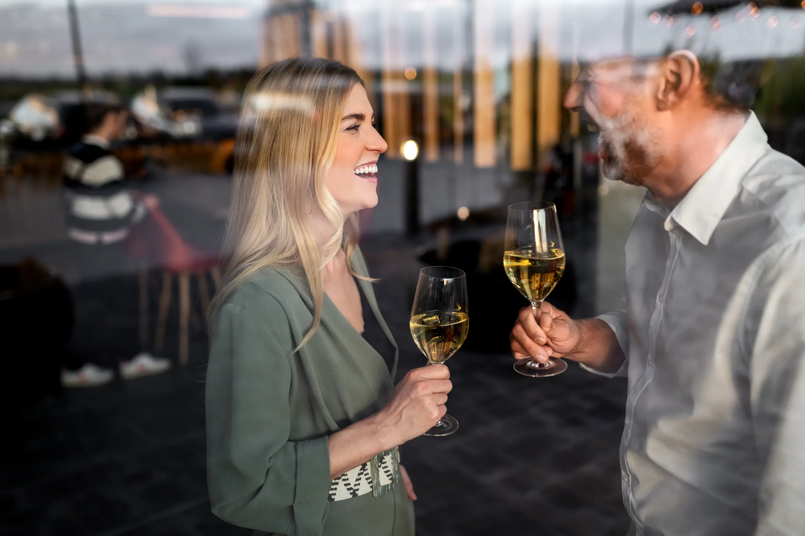 Ein Mann und eine Frau stehen sich lachend gegenüber und halten Weingläser