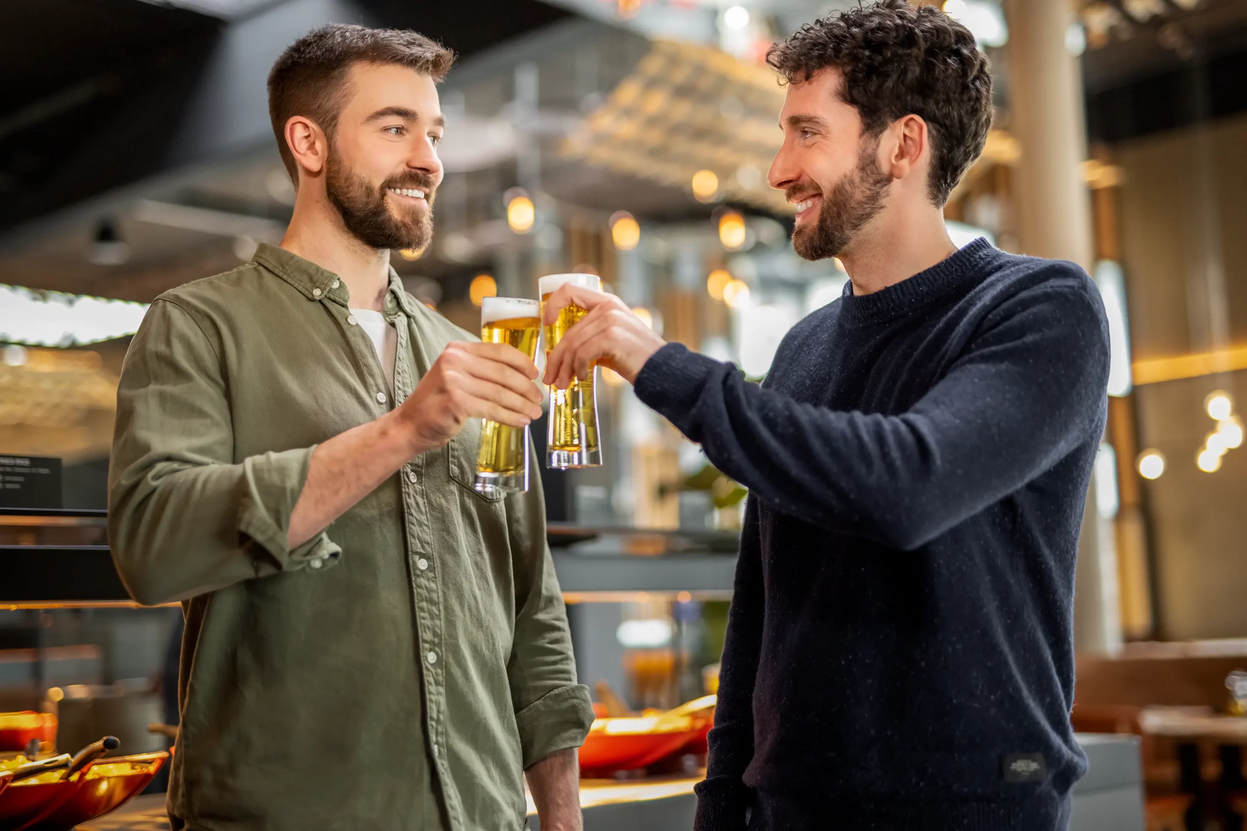 Zwei Freunde stoßen bei einem Event zusammen mit Bier am Buffet an