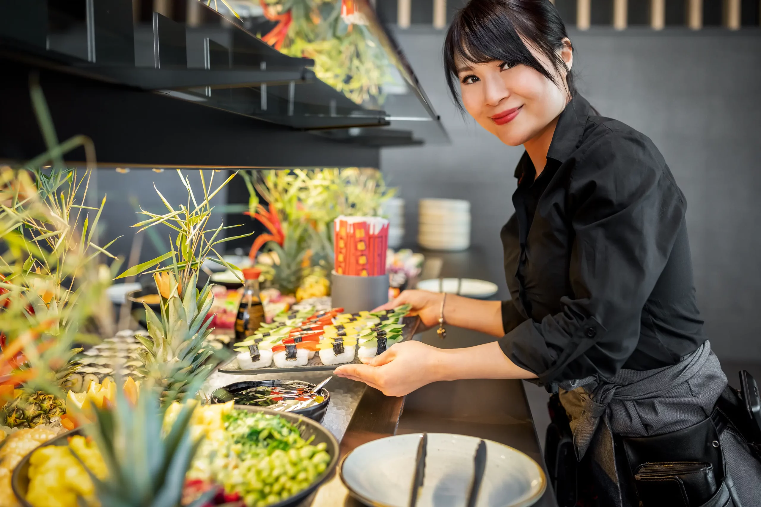 Eine Servicekraft am bunt gemischten Buffet mit veganem Sushi, Bowls und frischen Zutaten